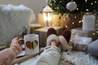 Photo of Woman with cup of cocoa in room decorated for Christmas, closeup