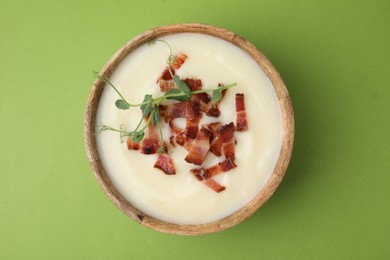 Delicious potato soup with bacon and microgreens in bowl on green table, top view