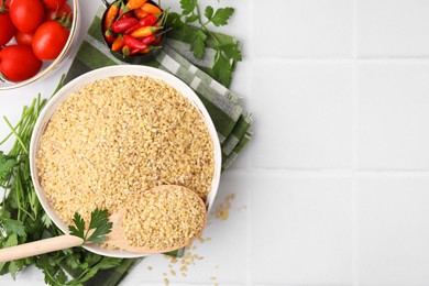 Photo of Raw bulgur in bowl, vegetables and parsley on white tiled table, flat lay. Space for text