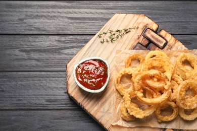 Homemade crunchy fried onion rings and sauce on wooden background, top view. Space for text