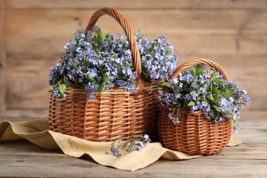 Beautiful forget-me-not flowers in wicker baskets on wooden table, closeup