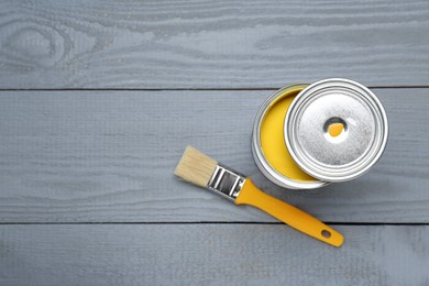 Photo of Can of yellow paint and brush on grey wooden table, flat lay. Space for text