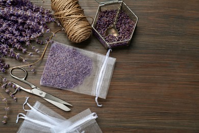 Scented sachet with dried lavender flowers, scissors and twine on wooden table, flat lay. Space for text