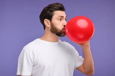 Photo of Man inflating red balloon on purple background