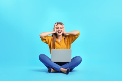 Emotional young woman with laptop celebrating victory on color background