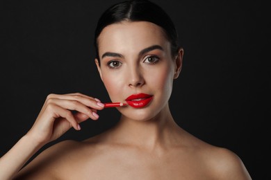 Photo of Pretty young woman with beautiful red lip pencil on black background