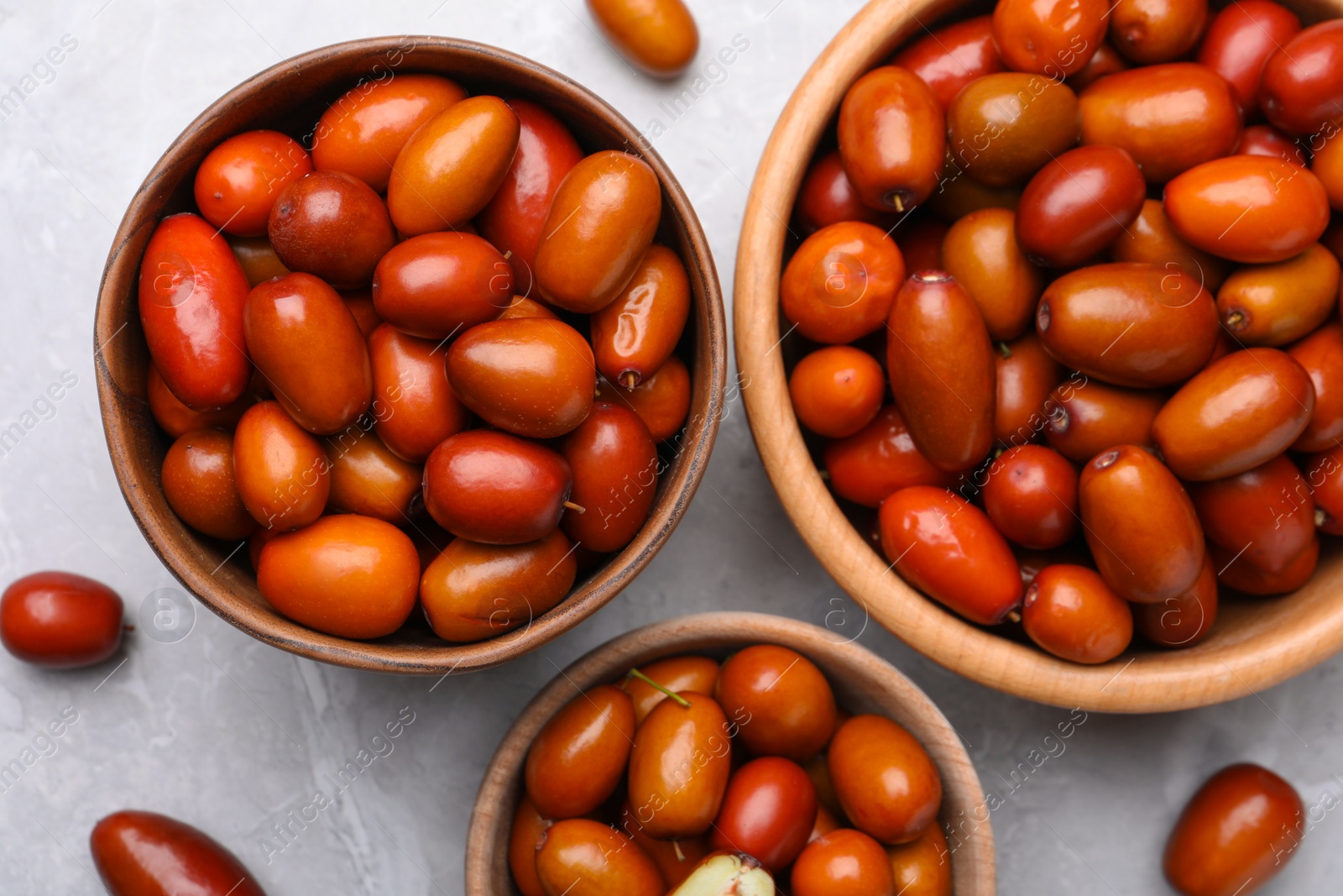 Photo of Fresh Ziziphus jujuba fruits with wooden bowls on light table, flat lay