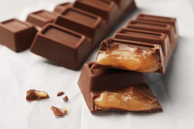 Photo of Tasty chocolate bars with caramel on paper, closeup view