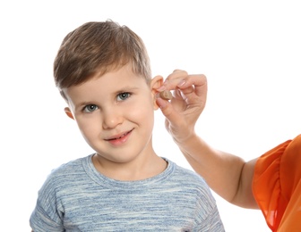 Mature woman putting hearing aid in little grandson's ear on white background, closeup