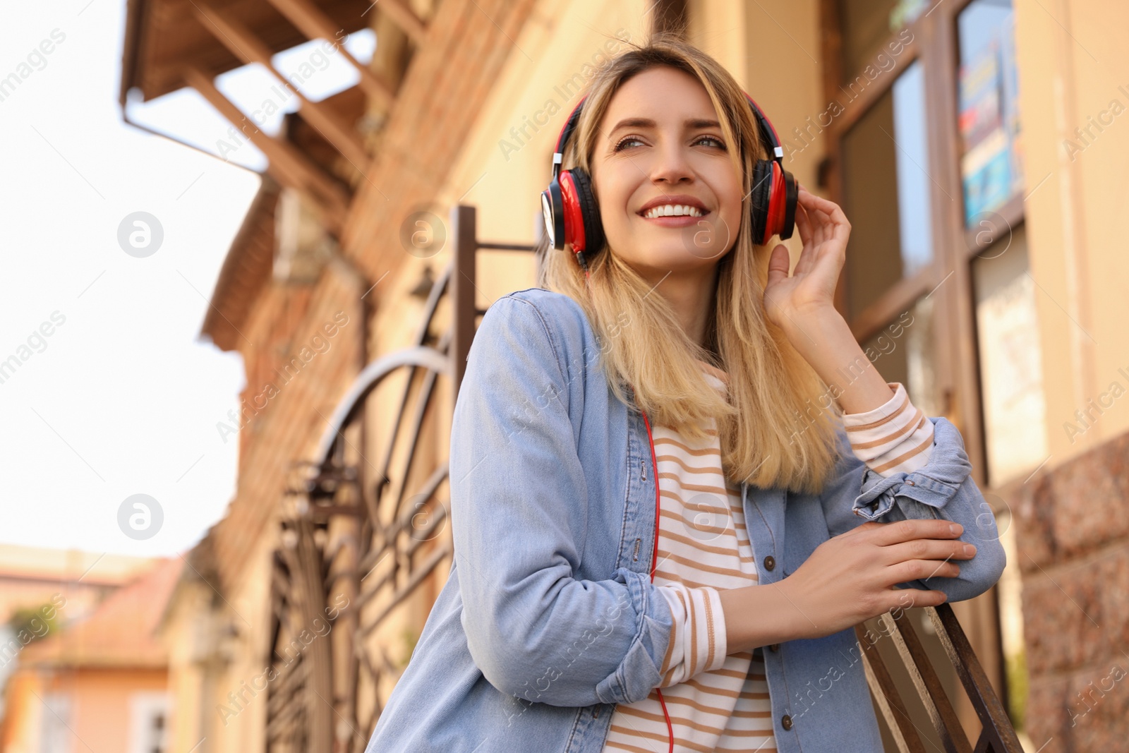 Photo of Happy young woman with headphones listening to music on city street