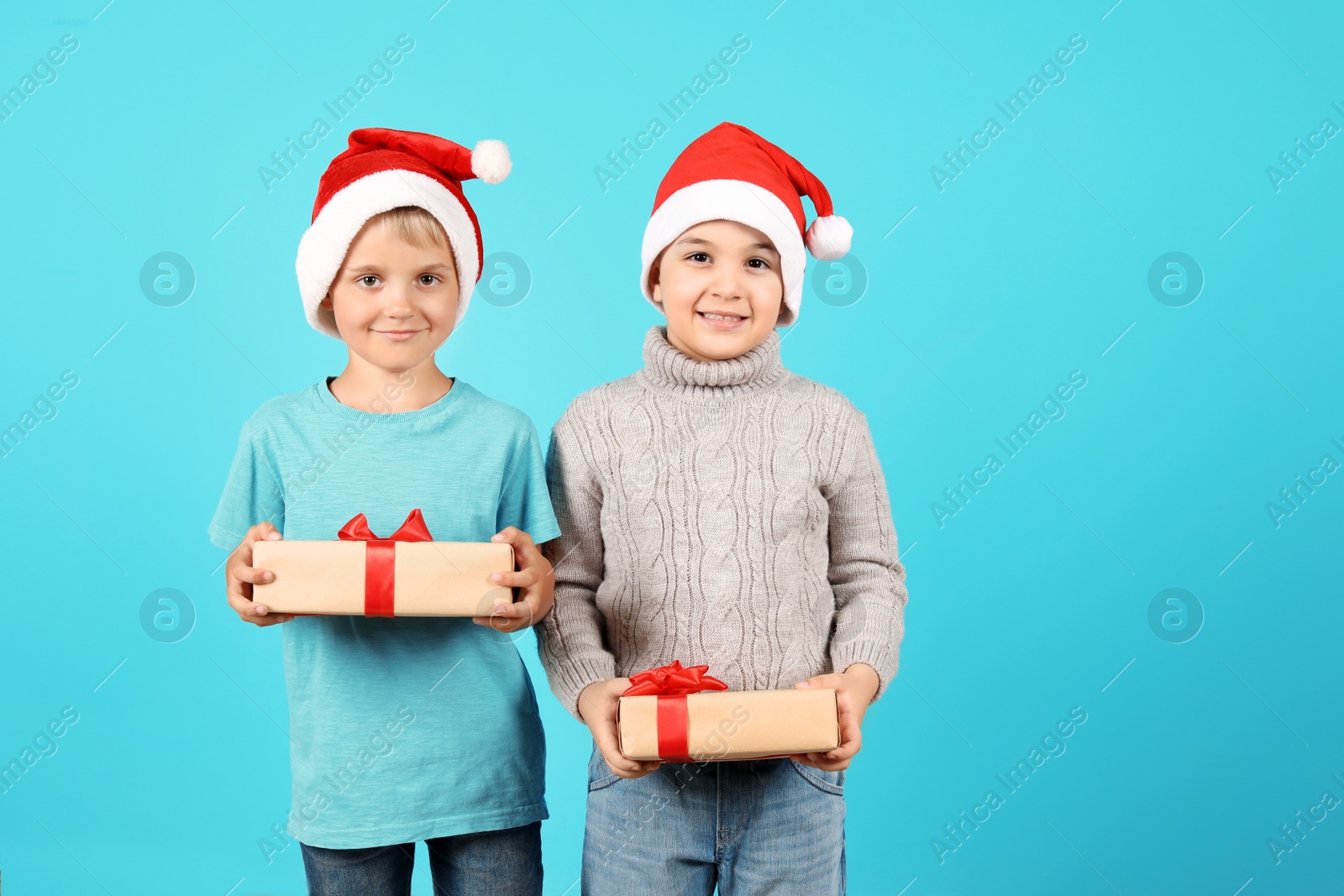 Photo of Cute little children in Santa hats with Christmas gifts on color background