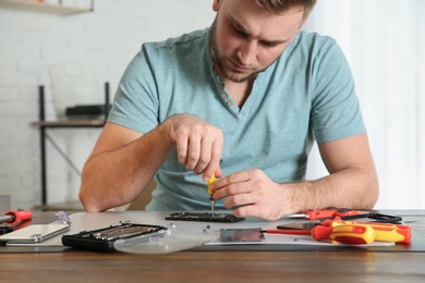 Photo of Young technician repairing mobile phone at table in workshop