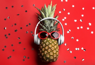 Photo of Pineapple with sunglasses, headphones and confetti on red background, flat lay. Creative concept