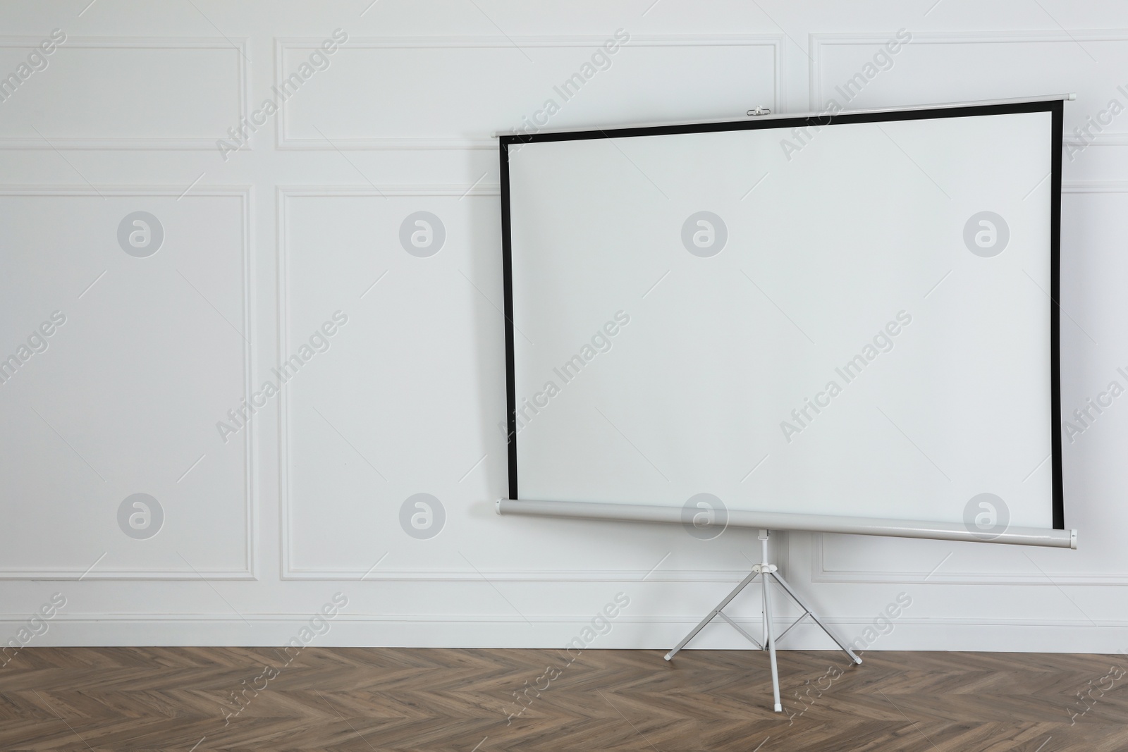 Photo of Blank projection screen near white wall indoors. Space for design