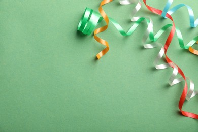 Photo of Colorful serpentine streamers on green background, flat lay. Space for text