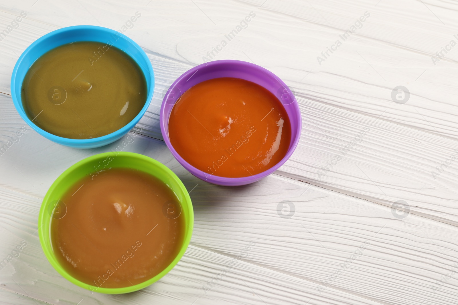 Photo of Baby food. Different purees in bowls on white wooden table. Space for text