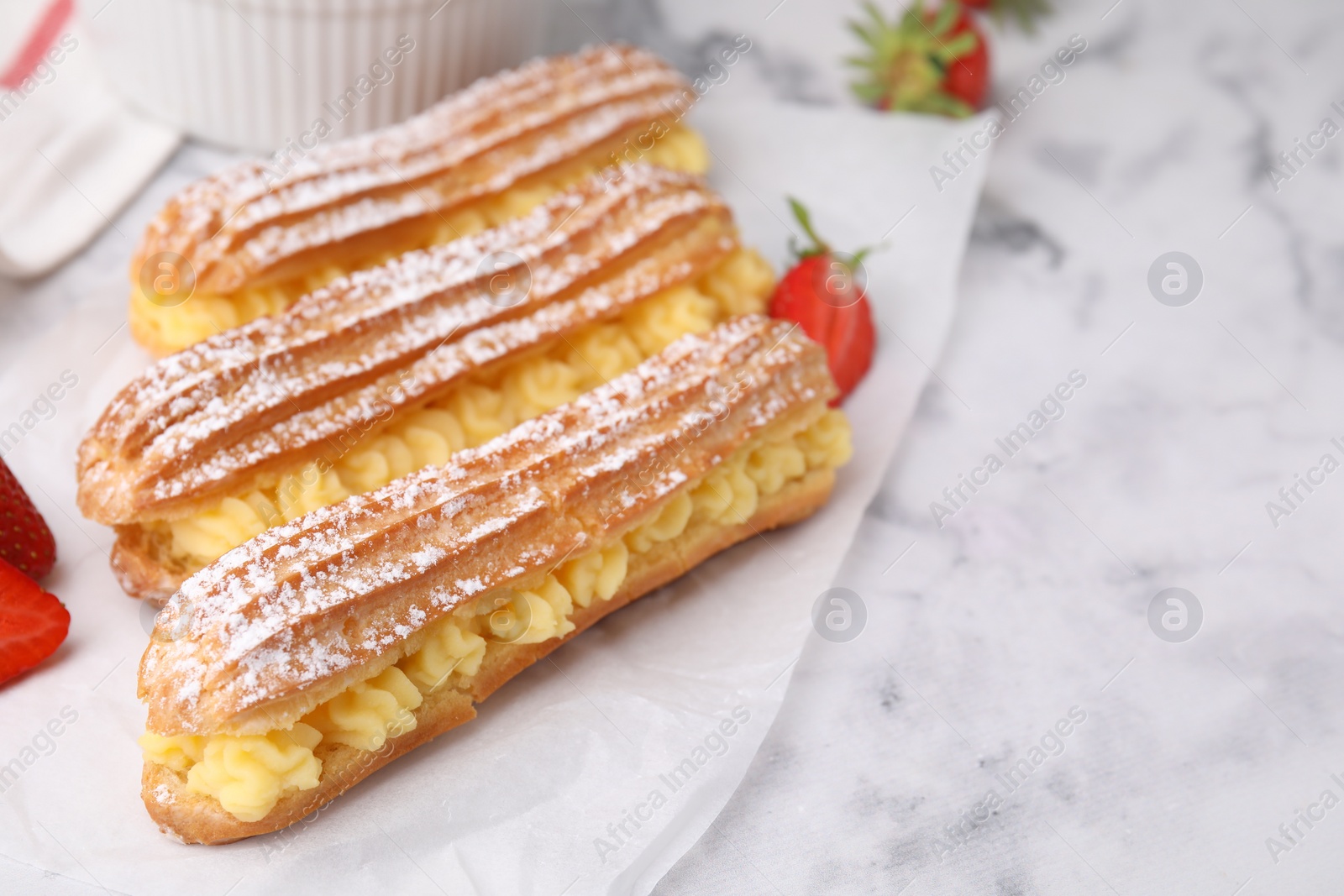 Photo of Delicious eclairs filled with cream and strawberries on white marble table, space for text