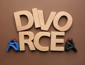 Photo of Word Divorce made of wooden letters and plasticine people figures on brown background, flat lay