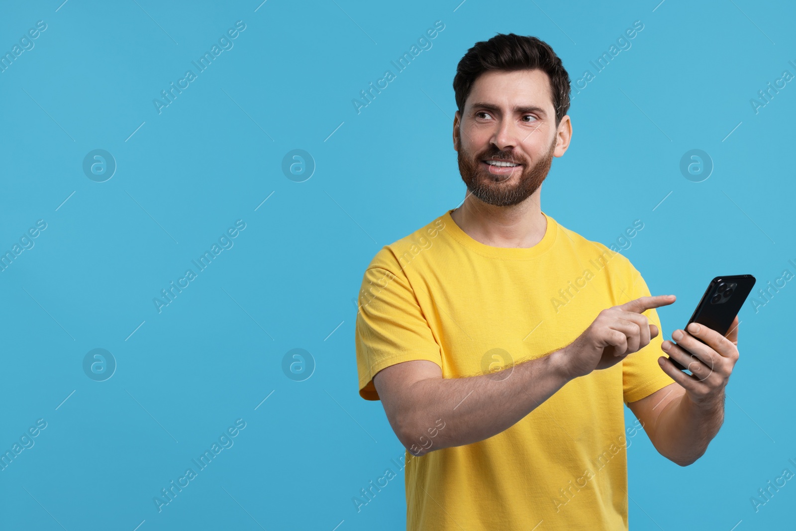 Photo of Happy man using smartphone on light blue background. Space for text