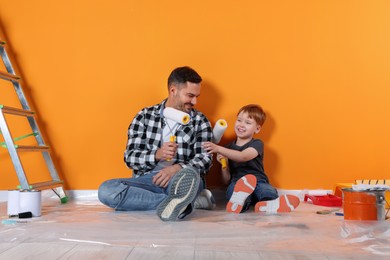 Father and son with rollers near orange wall. Repair work