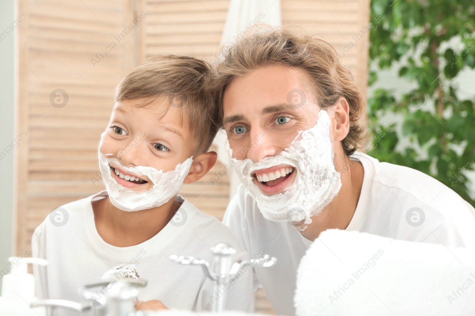 Photo of Father and son having fun with shaving foam on faces in bathroom