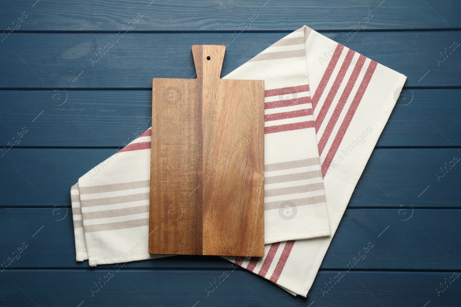 Photo of Striped kitchen towel and cutting board on blue wooden table, top view