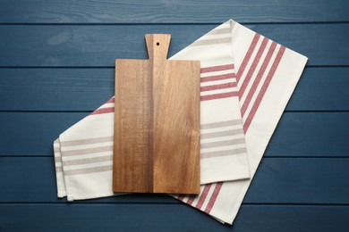 Photo of Striped kitchen towel and cutting board on blue wooden table, top view