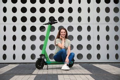 Happy woman sitting on modern electric kick scooter on city street