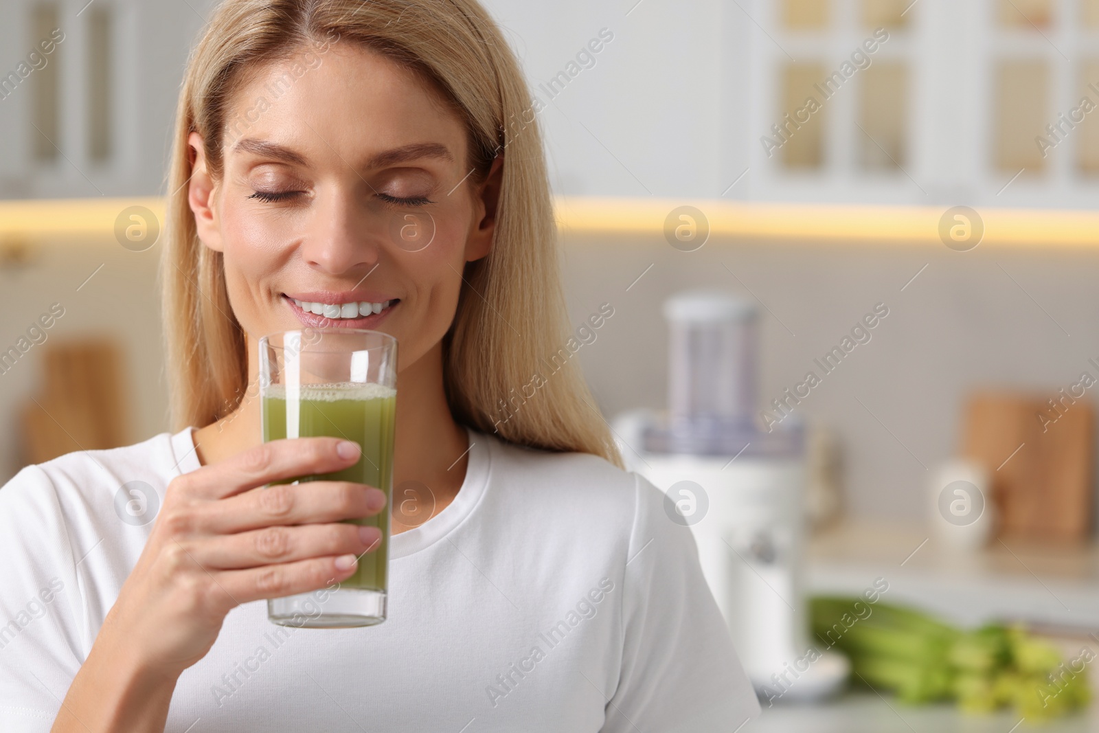 Photo of Woman drinking fresh celery juice in kitchen. Space for text