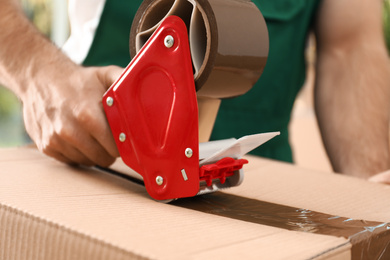 Photo of Man packing box with adhesive tape indoors, closeup. Moving service