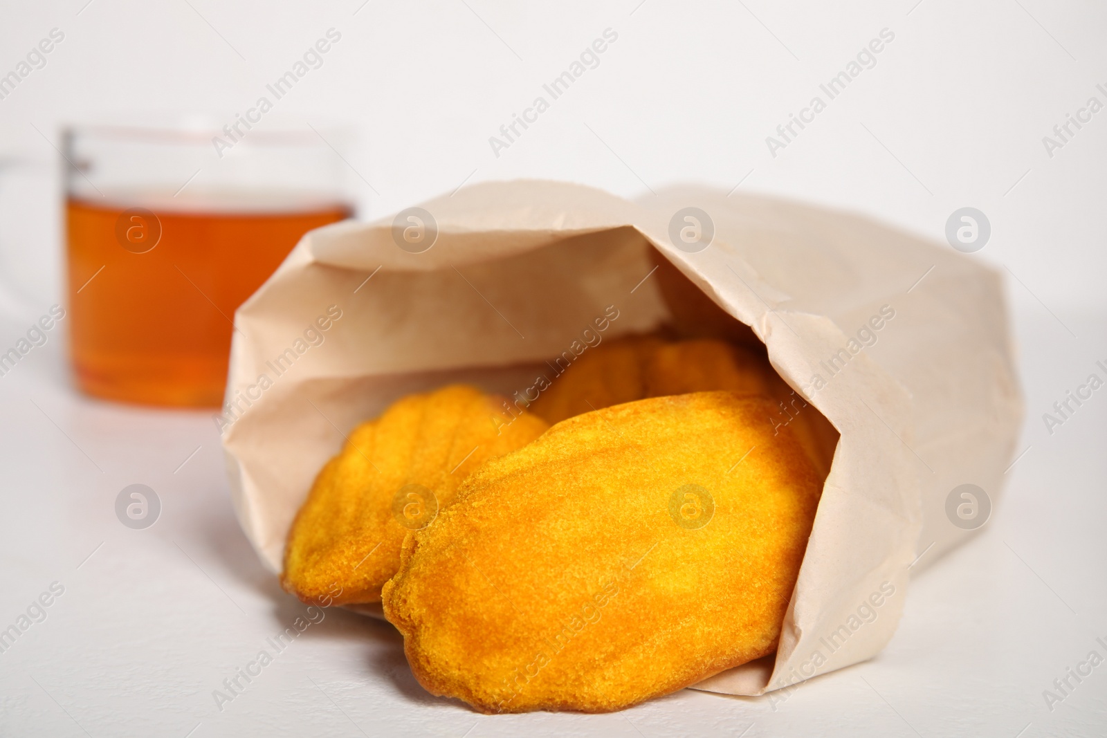 Photo of Paper bag with delicious madeleine cakes and cup of tea on white background, closeup