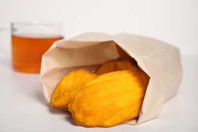 Photo of Paper bag with delicious madeleine cakes and cup of tea on white background, closeup