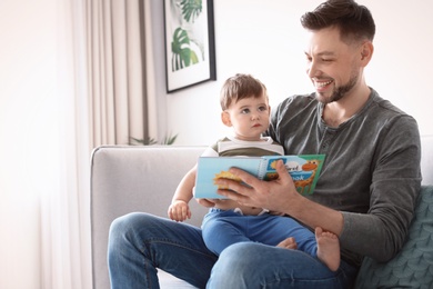 Photo of Dad and his son reading book on sofa at home