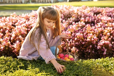 Cute little girl with basket of Easter eggs in park