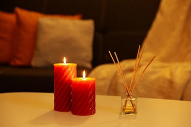 Photo of Beautiful candles and reed air freshener on white table indoors. Cosy atmosphere