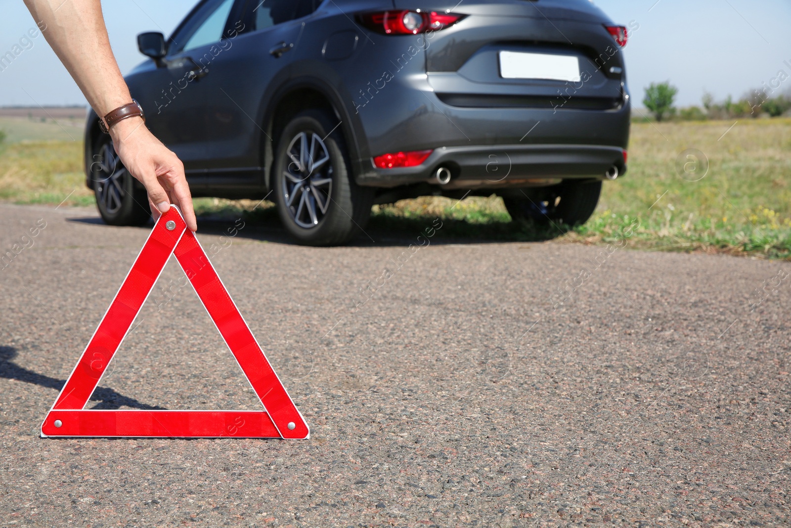 Photo of Man putting emergency stop sign near broken car on country road