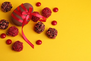 Photo of Tasty chocolate egg with red ribbon and candies on yellow background, flat lay. Space for text