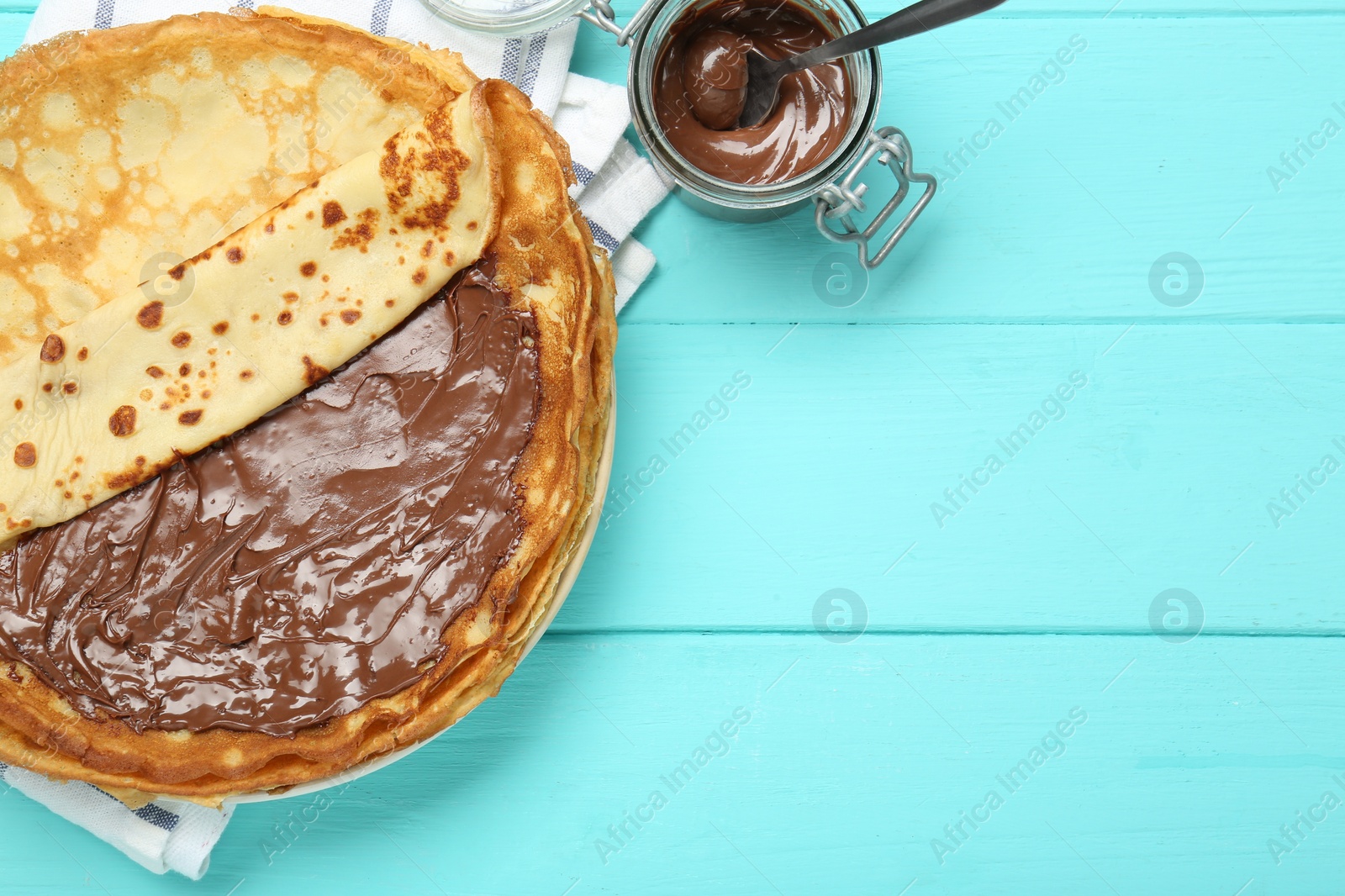 Photo of Tasty crepes with chocolate paste served on turquoise wooden table, flat lay. Space for text
