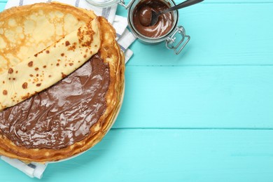 Tasty crepes with chocolate paste served on turquoise wooden table, flat lay. Space for text