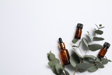 Aromatherapy. Bottles of essential oil and eucalyptus branches on white background, flat lay. Space for text