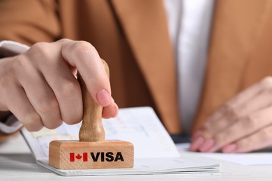 Image of Woman stamping document at white wooden table, closeup. Visa for Canada