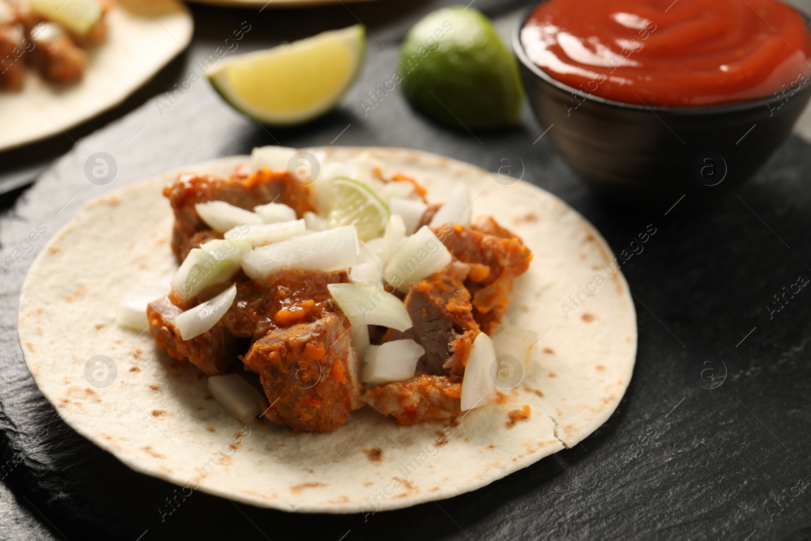 Photo of Delicious taco with vegetables, meat and lime on dark textured table, closeup