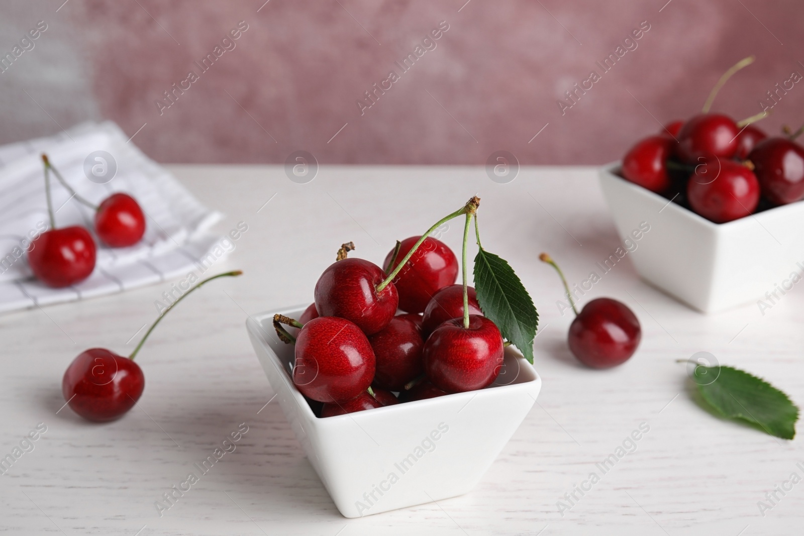 Photo of Bowl with ripe sweet cherries on white wooden table. Space for text