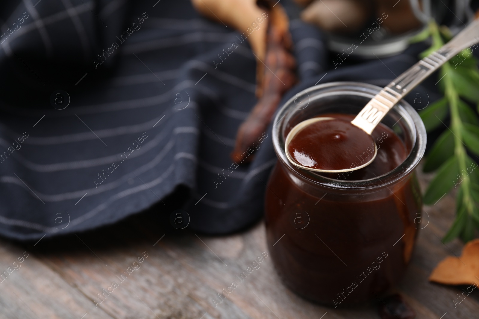 Jar of tasty tamarind sauce, spoon and fresh pods on wooden table. Space for text Photo of Jar of tasty tamarind sauce, spoon and fresh pods on wooden table. Space for text