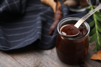 Photo of Jar of tasty tamarind sauce, spoon and fresh pods on wooden table. Space for text