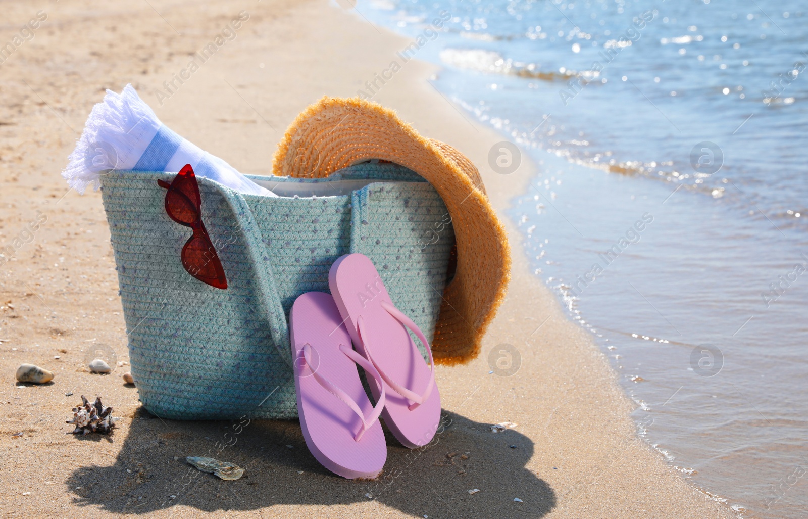 Photo of Bag with beach accessories and flip flops on sand near sea