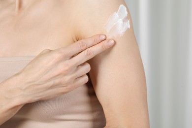 Photo of Woman applying body cream onto arm on blurred background, closeup