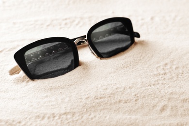 Stylish sunglasses on white sand. Space for text