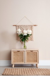 Wooden chest of drawers with bouquet near beige wall indoors