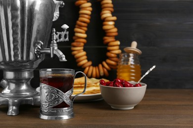 Photo of Metal samovar with cuptea and treats on wooden table